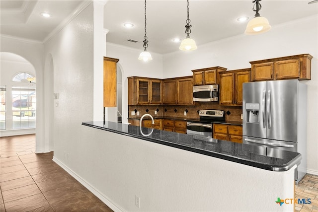 kitchen featuring dark countertops, brown cabinetry, arched walkways, and appliances with stainless steel finishes