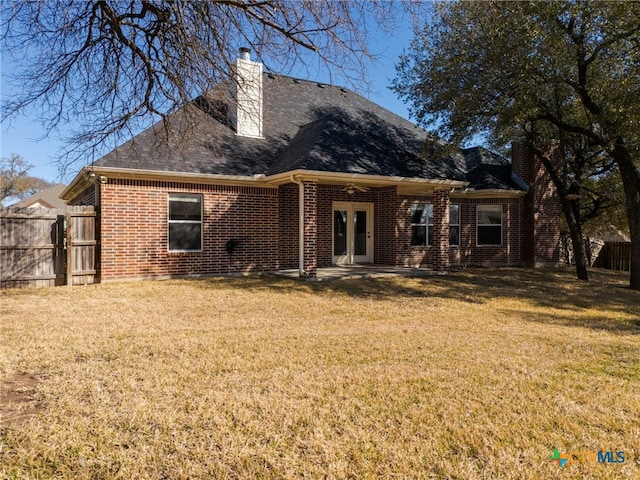 rear view of property featuring a lawn, fence, french doors, brick siding, and a chimney