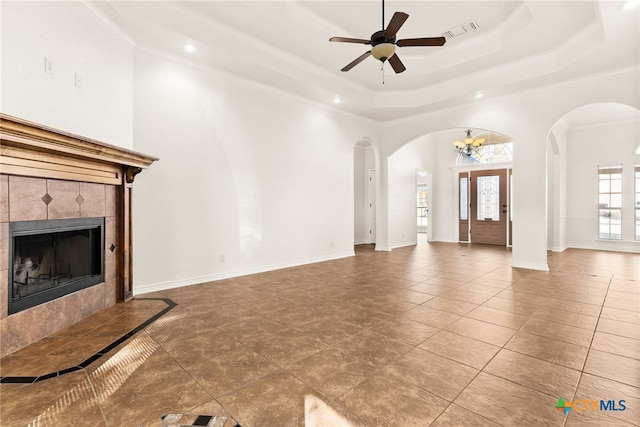 unfurnished living room with visible vents, ceiling fan with notable chandelier, arched walkways, a fireplace, and baseboards