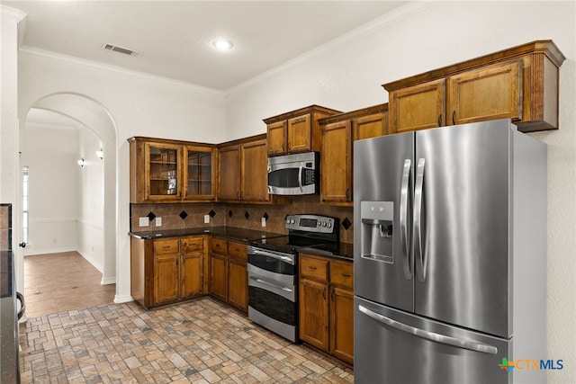 kitchen featuring arched walkways, brown cabinets, appliances with stainless steel finishes, and crown molding