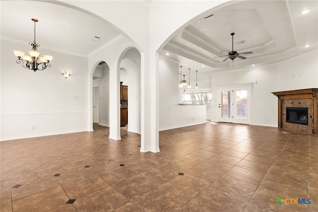 unfurnished living room with a raised ceiling, ceiling fan with notable chandelier, crown molding, baseboards, and a tile fireplace