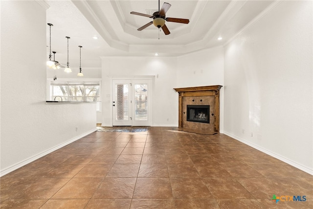 unfurnished living room featuring a tiled fireplace, a tray ceiling, a ceiling fan, and baseboards