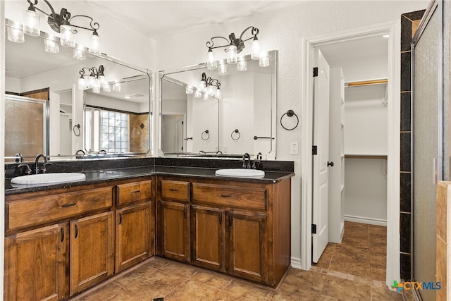 full bath with double vanity, a shower stall, a walk in closet, and a sink