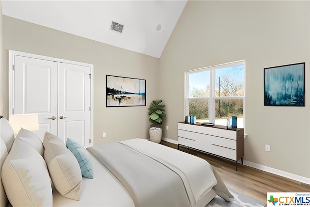 bedroom with hardwood / wood-style floors, high vaulted ceiling, and a closet