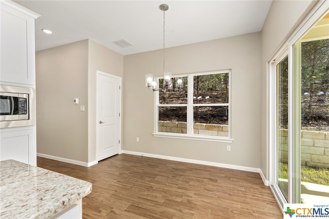 unfurnished dining area with wood-type flooring and an inviting chandelier