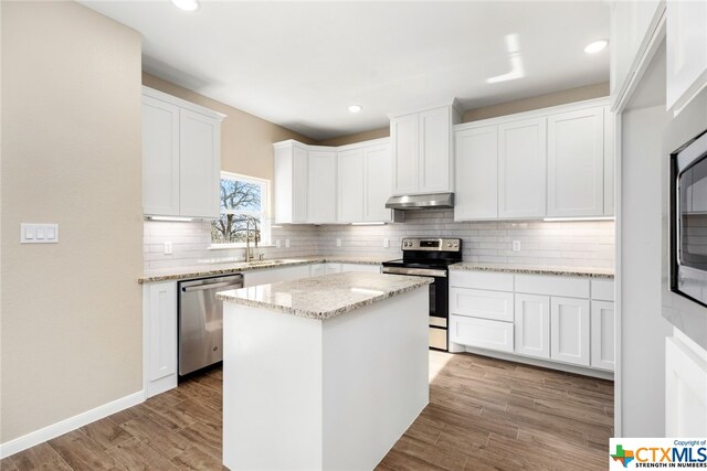 kitchen featuring a center island, light hardwood / wood-style flooring, appliances with stainless steel finishes, light stone counters, and white cabinetry