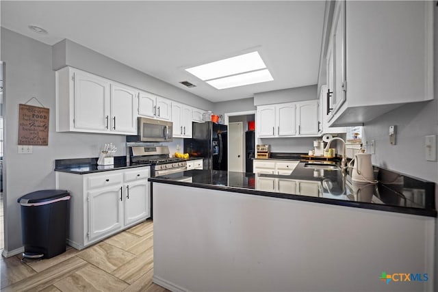 kitchen with appliances with stainless steel finishes, a sink, a peninsula, dark countertops, and white cabinetry