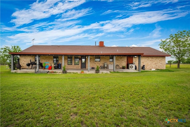 rear view of property featuring a patio, a chimney, a yard, and brick siding
