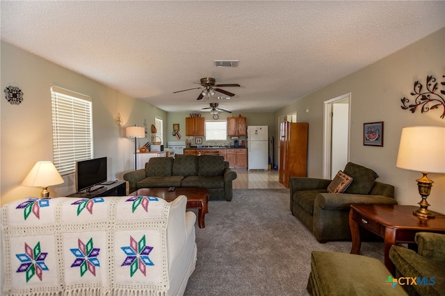 carpeted living room with a textured ceiling and ceiling fan