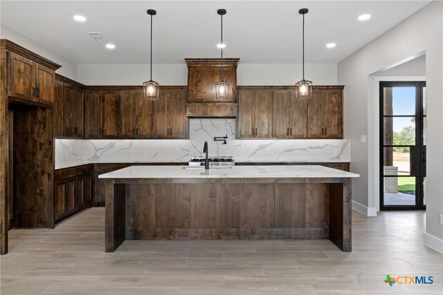 644 Creekside Dr, Belton, TX 76513 - kitchen with decorative backsplash, premium range hood, a kitchen island with sink, light wood-style floors, and decorative light fixtures