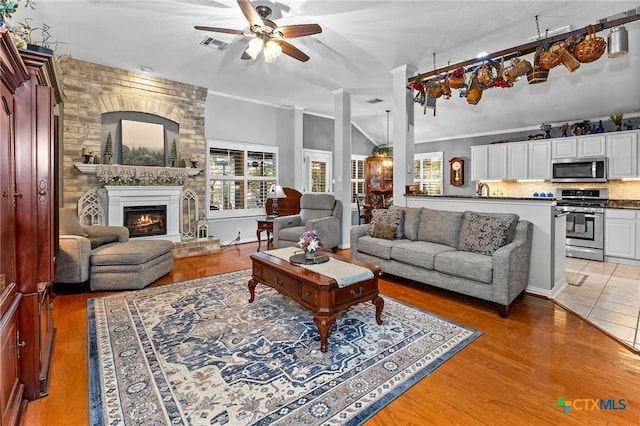 living room with ceiling fan, wood-type flooring, vaulted ceiling, and a brick fireplace