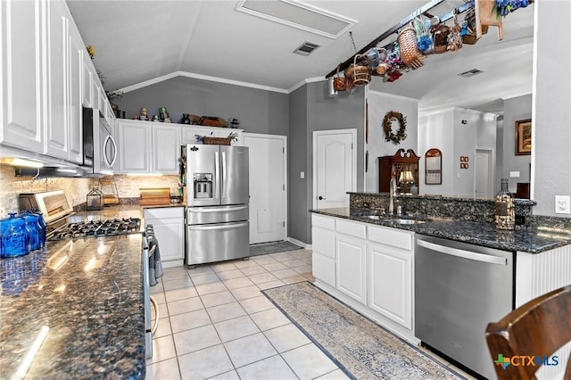 kitchen featuring light tile patterned flooring, vaulted ceiling, appliances with stainless steel finishes, dark stone counters, and white cabinets