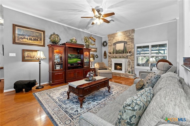 living room featuring wood-type flooring, ornamental molding, a large fireplace, and ceiling fan