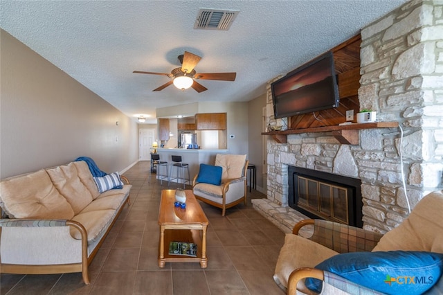 tiled living room with a stone fireplace, a textured ceiling, ceiling fan, and vaulted ceiling