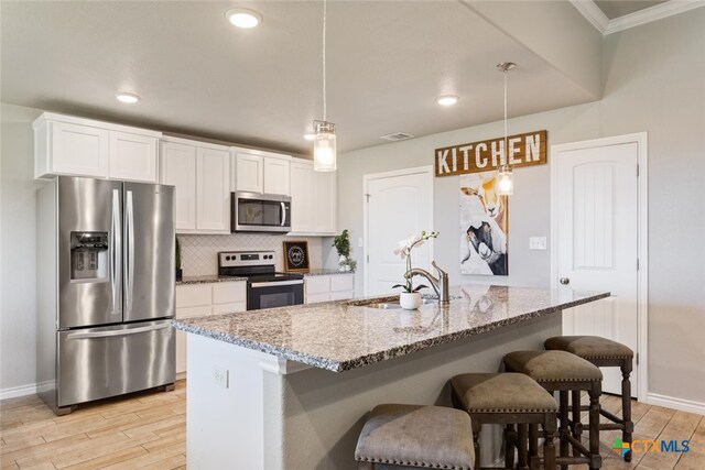 kitchen featuring white cabinetry, appliances with stainless steel finishes, an island with sink, and hanging light fixtures