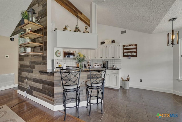 kitchen featuring tasteful backsplash, dark countertops, visible vents, lofted ceiling with beams, and white cabinets