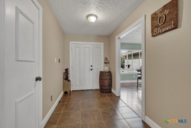 interior space featuring baseboards, a textured ceiling, and dark tile patterned flooring