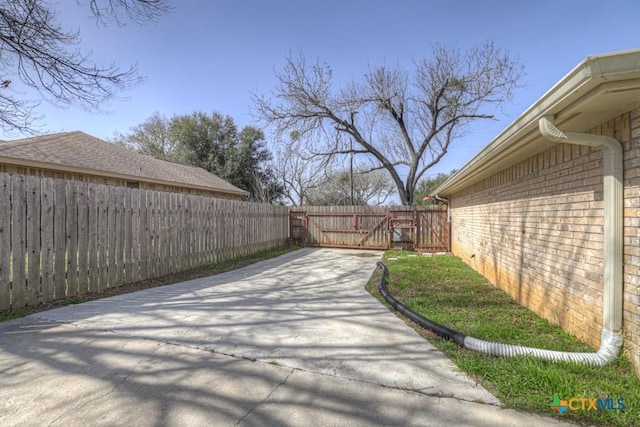 view of yard with concrete driveway, fence, and a gate