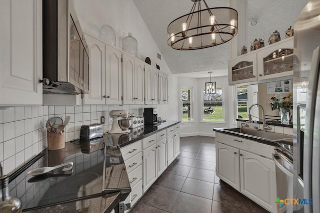 kitchen with dark countertops, lofted ceiling, stove, a chandelier, and backsplash