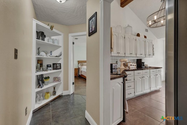 interior space featuring lofted ceiling with beams, a textured ceiling, built in shelves, dark tile patterned floors, and an inviting chandelier