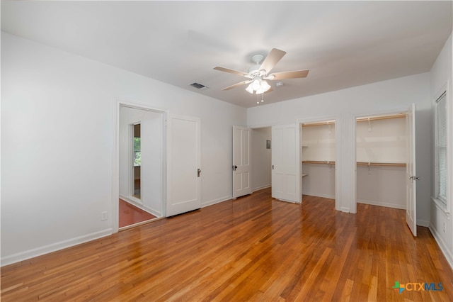 unfurnished bedroom featuring ceiling fan, multiple closets, and light wood-type flooring