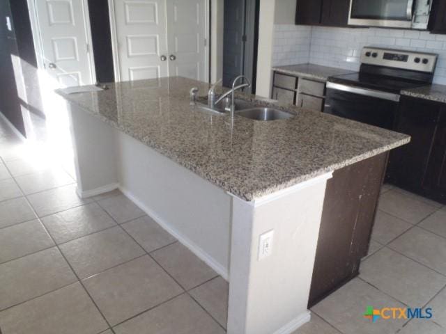 kitchen featuring appliances with stainless steel finishes, backsplash, light stone counters, sink, and an island with sink