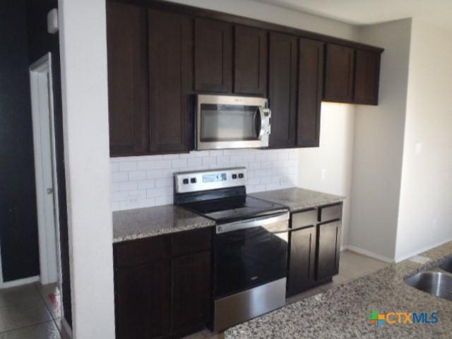 kitchen featuring decorative backsplash, light stone counters, dark brown cabinets, and appliances with stainless steel finishes