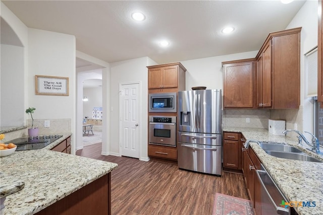 kitchen with sink, decorative backsplash, stainless steel appliances, light stone countertops, and dark wood-type flooring