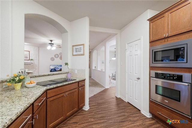 kitchen featuring appliances with stainless steel finishes, decorative backsplash, ceiling fan, light stone countertops, and dark wood-type flooring