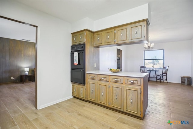 kitchen with brown cabinets, light wood finished floors, light countertops, dobule oven black, and a peninsula