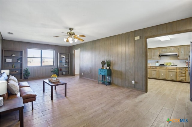 living room with light wood finished floors, visible vents, built in features, and a ceiling fan