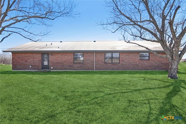 back of house featuring brick siding, metal roof, and a yard