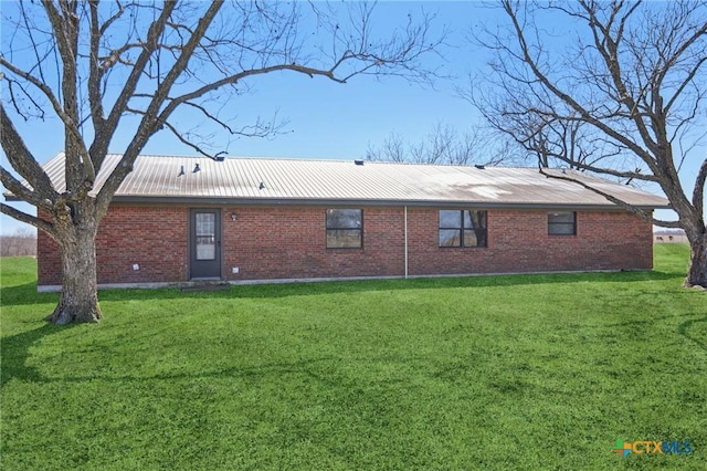 rear view of property featuring metal roof, brick siding, and a lawn