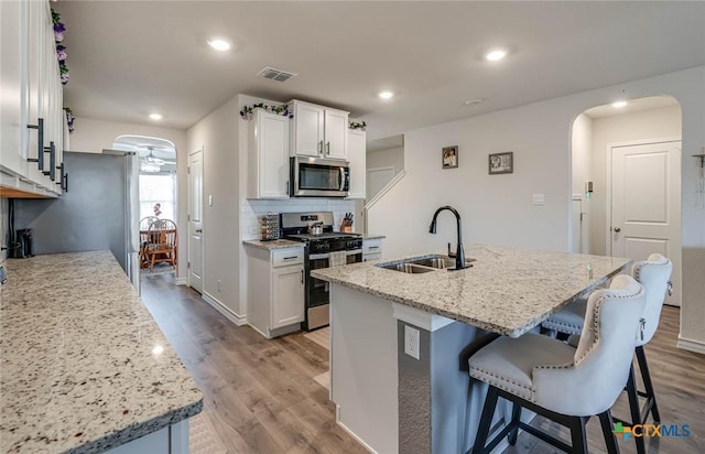 kitchen with an island with sink, sink, white cabinets, hardwood / wood-style flooring, and stainless steel appliances