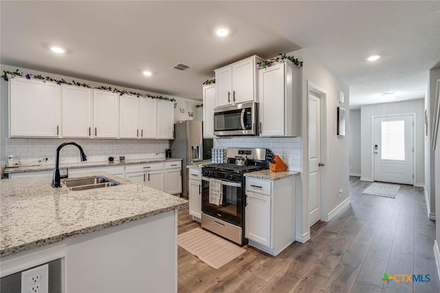 kitchen featuring sink, light wood-type flooring, stainless steel appliances, light stone countertops, and white cabinets