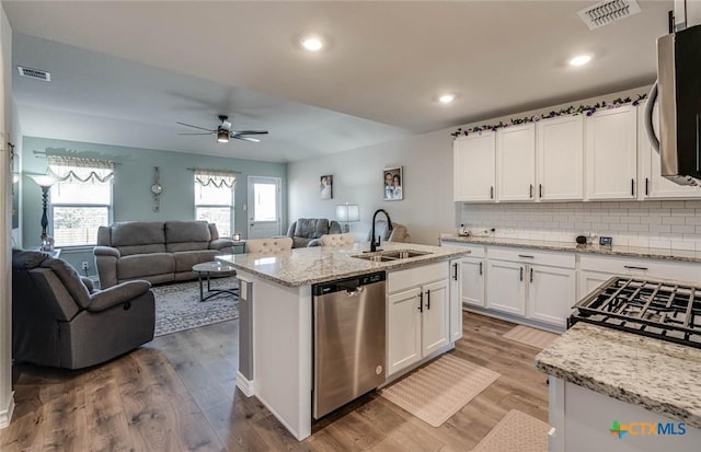 kitchen with sink, stainless steel appliances, light stone counters, an island with sink, and white cabinets