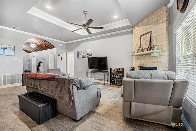 1211 Liberation Ln, Copperas Cove, TX 76522 - living area featuring ceiling fan, a tray ceiling, arched walkways, crown molding, and a stone fireplace