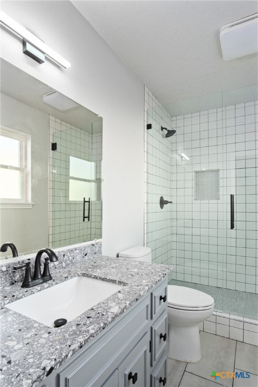 bathroom featuring toilet, vanity, tile patterned flooring, and a shower with shower door