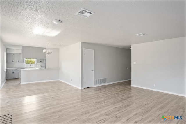 unfurnished living room featuring light wood-type flooring, a notable chandelier, and a textured ceiling