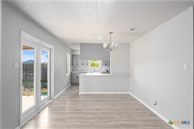 kitchen featuring a textured ceiling, kitchen peninsula, hanging light fixtures, and light hardwood / wood-style flooring