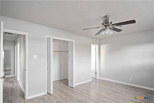 unfurnished bedroom with ceiling fan, a textured ceiling, a walk in closet, a closet, and light wood-type flooring