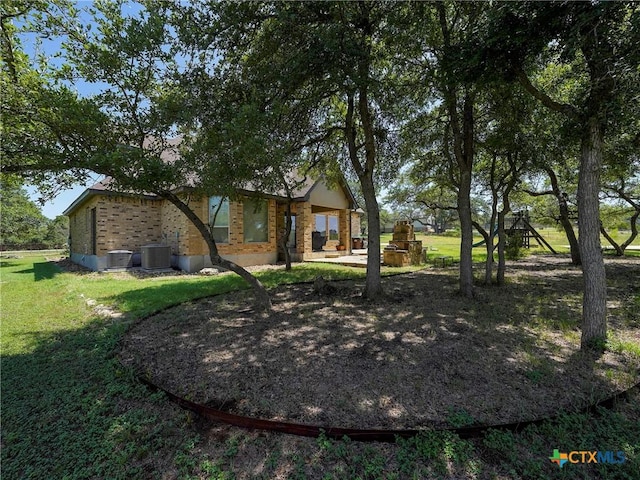 rear view of house with central AC, a lawn, and brick siding