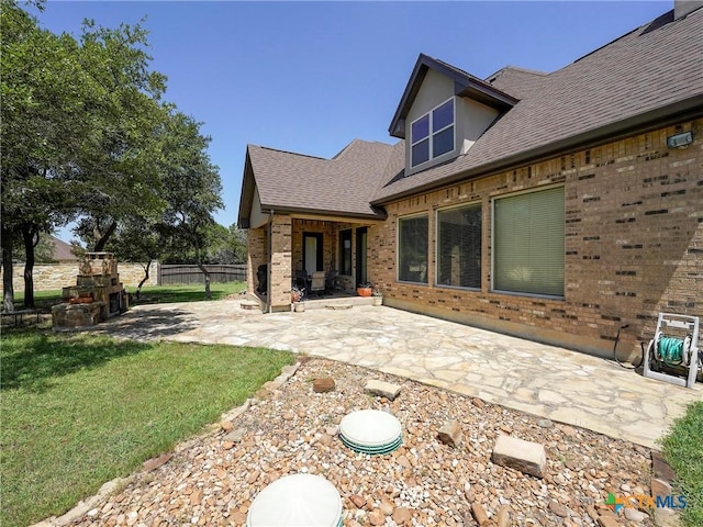 back of property featuring a patio area, brick siding, roof with shingles, and a fireplace