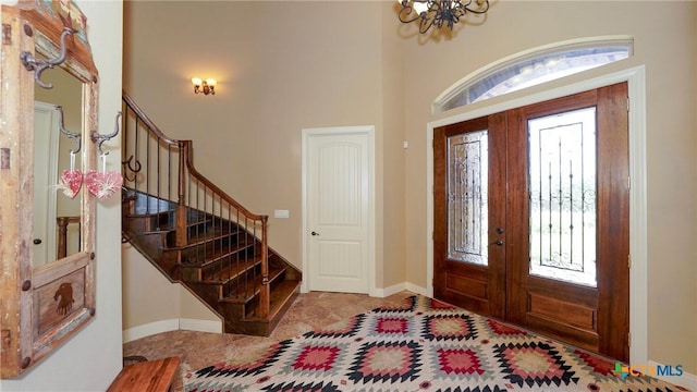entryway featuring a chandelier, stairs, baseboards, a high ceiling, and french doors