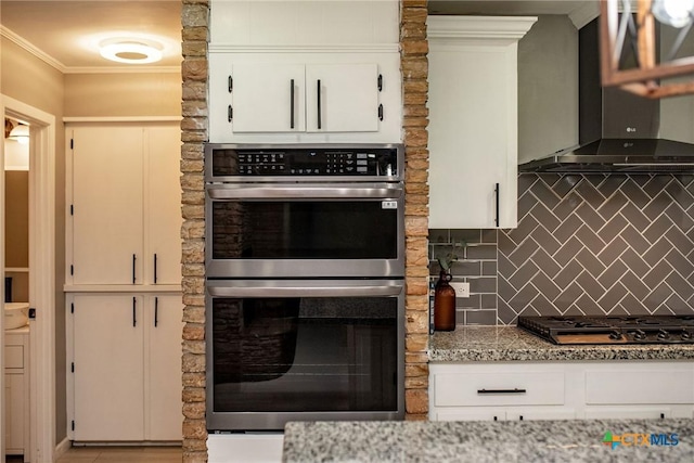 kitchen with decorative backsplash, crown molding, stainless steel double oven, wall chimney range hood, and gas stovetop