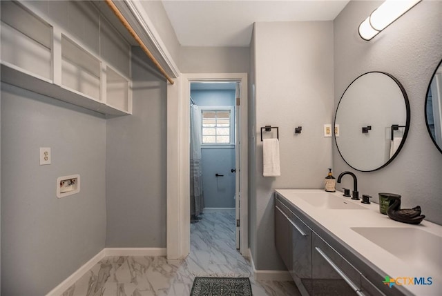 bathroom featuring double vanity, marble finish floor, baseboards, and a sink