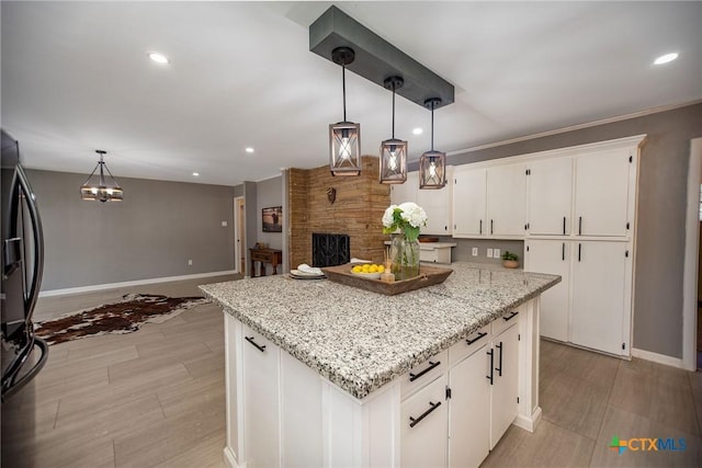 kitchen with a center island, pendant lighting, white cabinets, light stone countertops, and black fridge