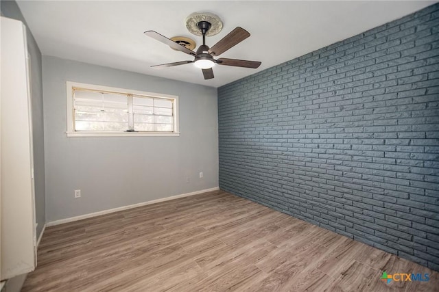 unfurnished room with ceiling fan, brick wall, light wood finished floors, and baseboards