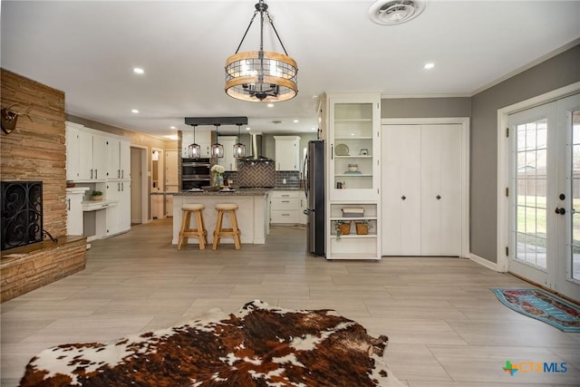 kitchen featuring visible vents, a kitchen breakfast bar, french doors, appliances with stainless steel finishes, and wall chimney range hood