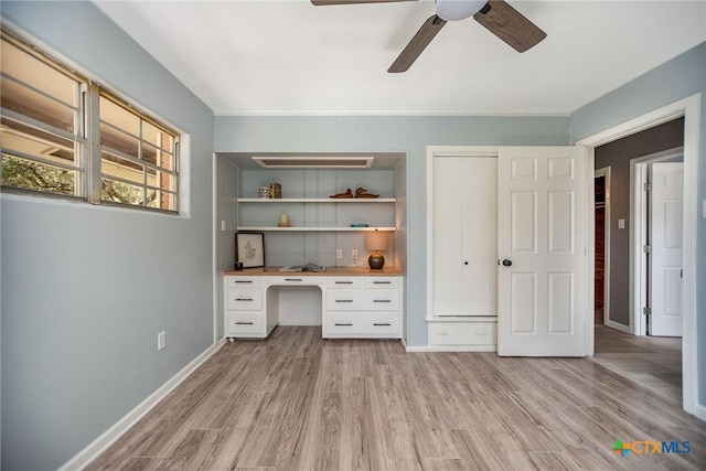 unfurnished office featuring baseboards, built in study area, ceiling fan, and light wood finished floors